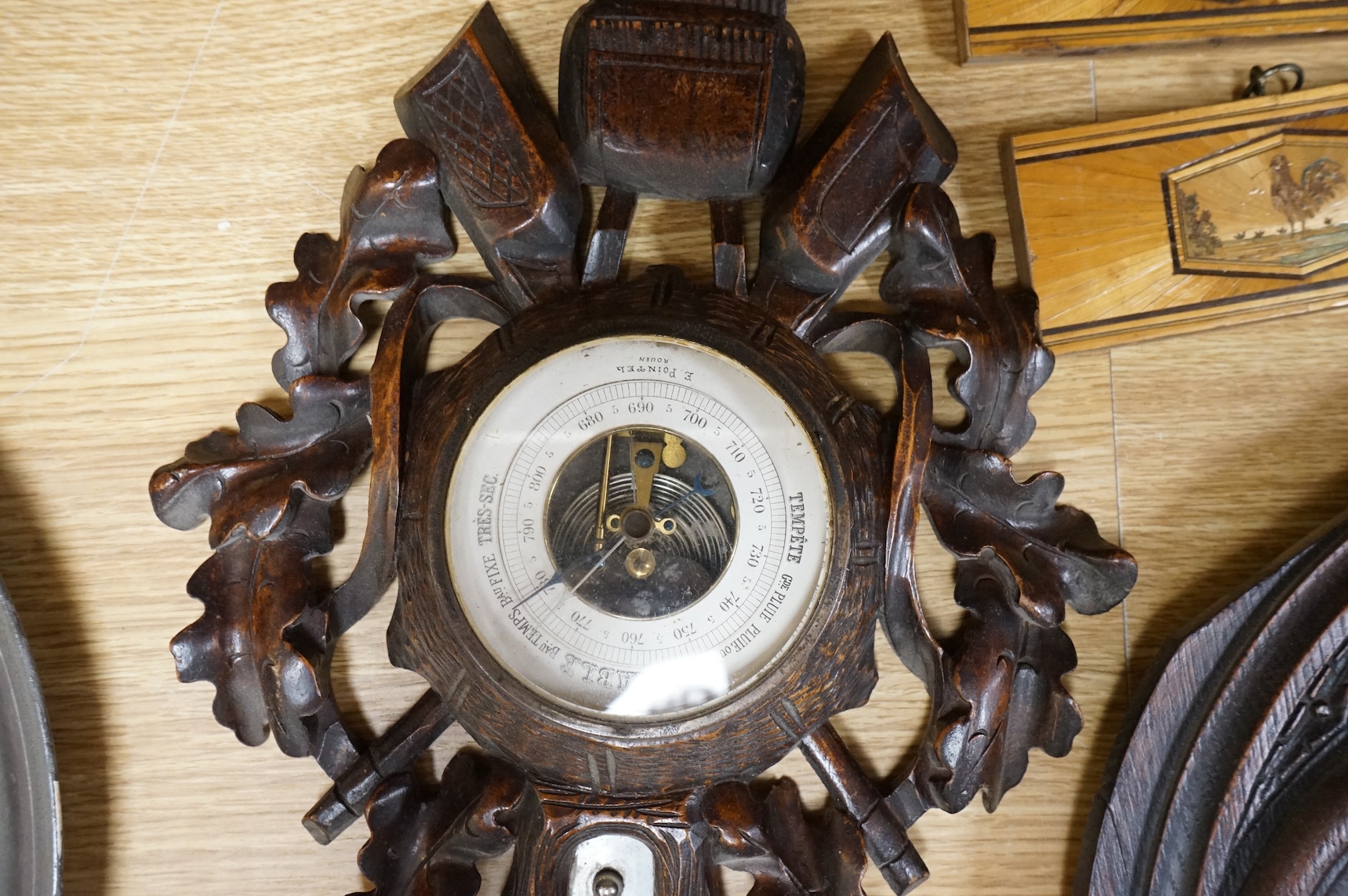 A pair of Gothic revival oak wall plaques, a Black Forest carved barometer, a Virgin and child figure, an IHS embroidered panel, two straw worked panels and a carved finial, barometer 47cm high